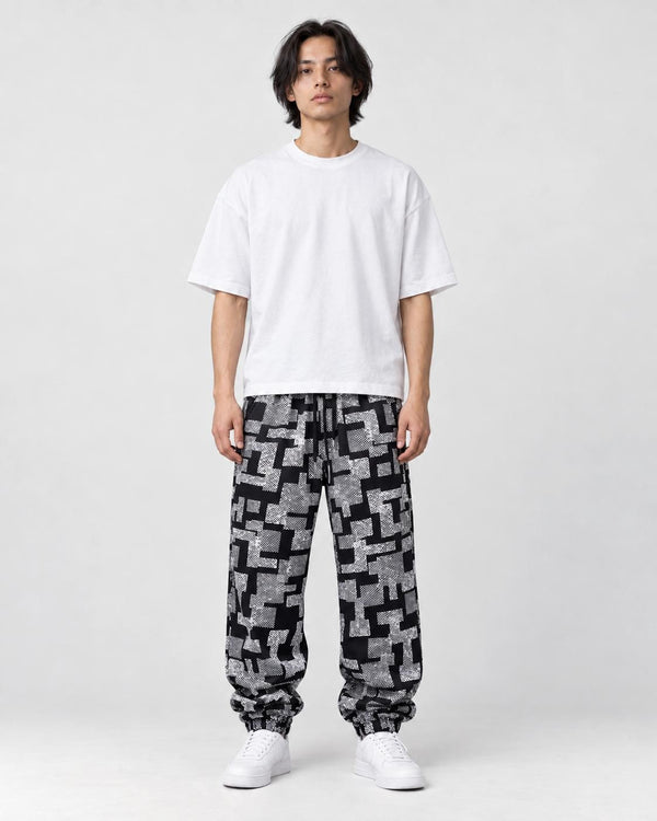 Man in black joggers with a white-gray maze block print, a white tee and white sneakers, full length