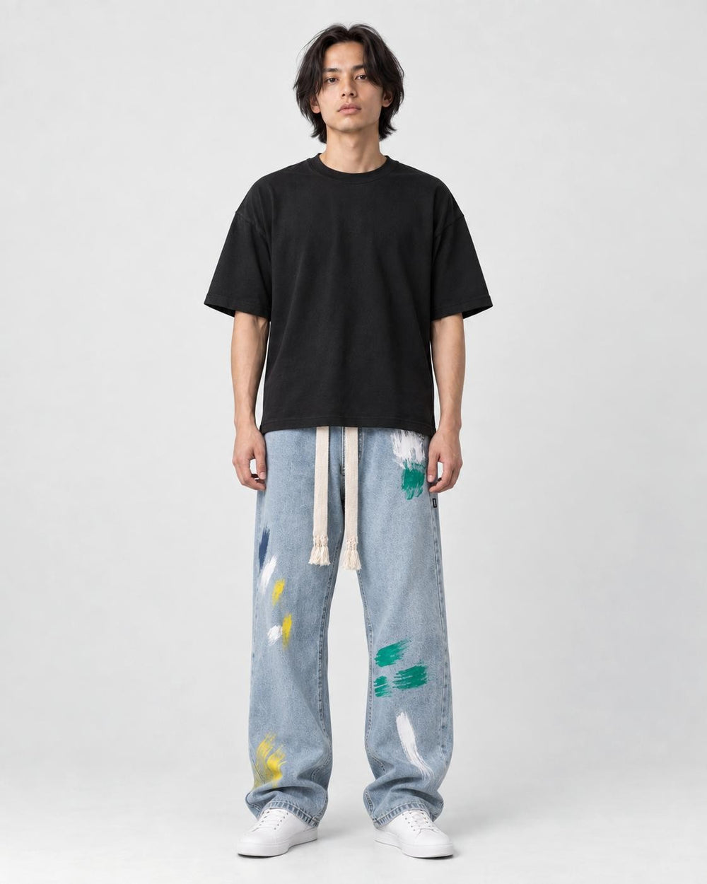 Model wearing the light blue paint-splatter wide-leg jeans with a black tee and white sneakers, front view