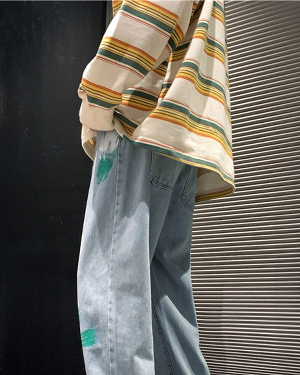 Man seated in the light blue paint-splatter jeans, showing the green and white paint streaks on the legs
