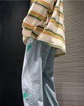 Man seated in the light blue paint-splatter jeans, showing the green and white paint streaks on the legs