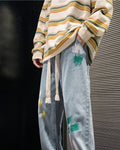 Light blue paint-splatter jeans with a green and white paint patch on the hip and long cotton tapes