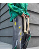 Washed gray wide-leg jeans with yellow, green, navy and white paint streaks, worn with a green sweatshirt