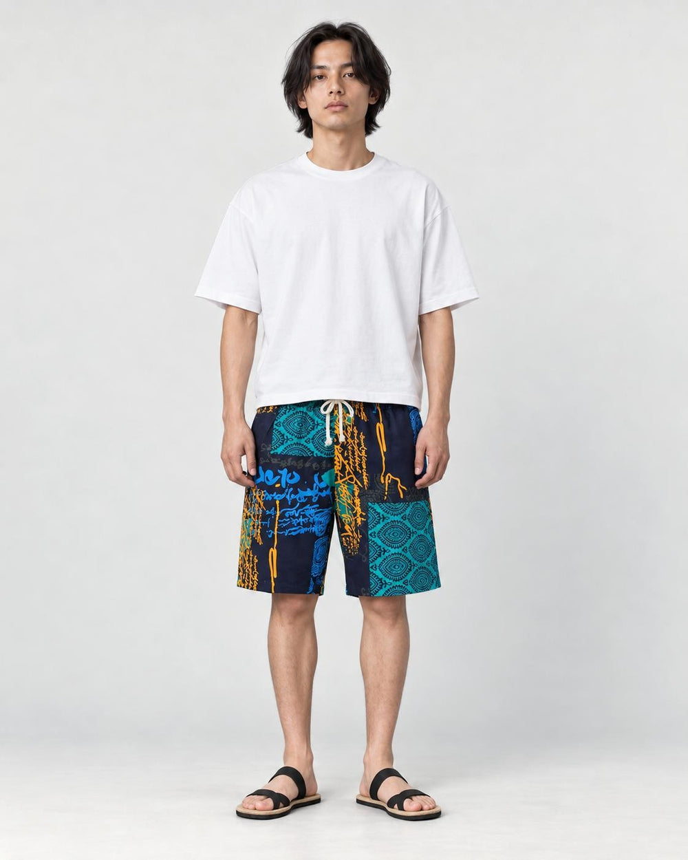 Model wearing the navy and teal patchwork print shorts with a white tee and black slides, front view
