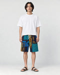 Model wearing the navy and teal patchwork print shorts with a white tee and black slides, front view