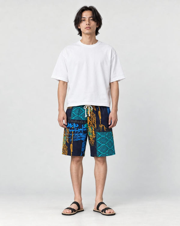 Model wearing the navy and teal patchwork print shorts with a white tee and black slides, front view