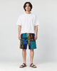 Model wearing the navy and teal patchwork print shorts with a white tee and black slides, front view