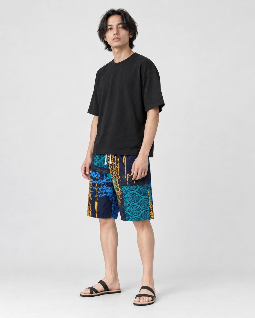 Model wearing the navy and teal patchwork print shorts with a black tee and black slides, three-quarter view