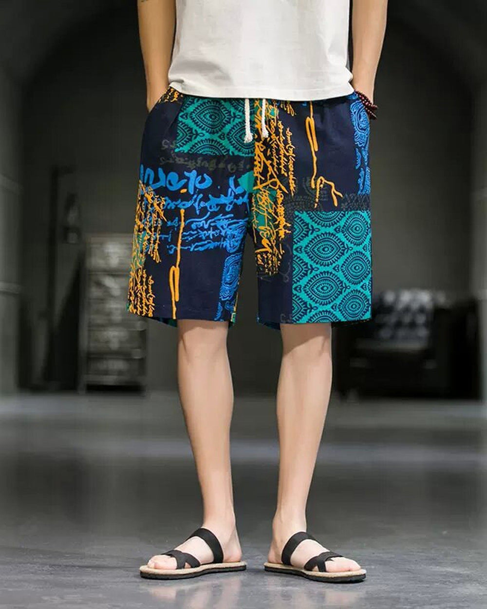 Navy and teal patchwork print shorts with white drawcords, worn with a white tee and black slides