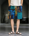 Navy and teal patchwork print shorts with white drawcords, worn with a white tee and black slides