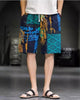 Navy and teal patchwork print shorts with hands in the side pockets and a large teal eye-shape panel