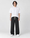Man in black plaid wide-leg drawstring pants, white tee and white sneakers, full length