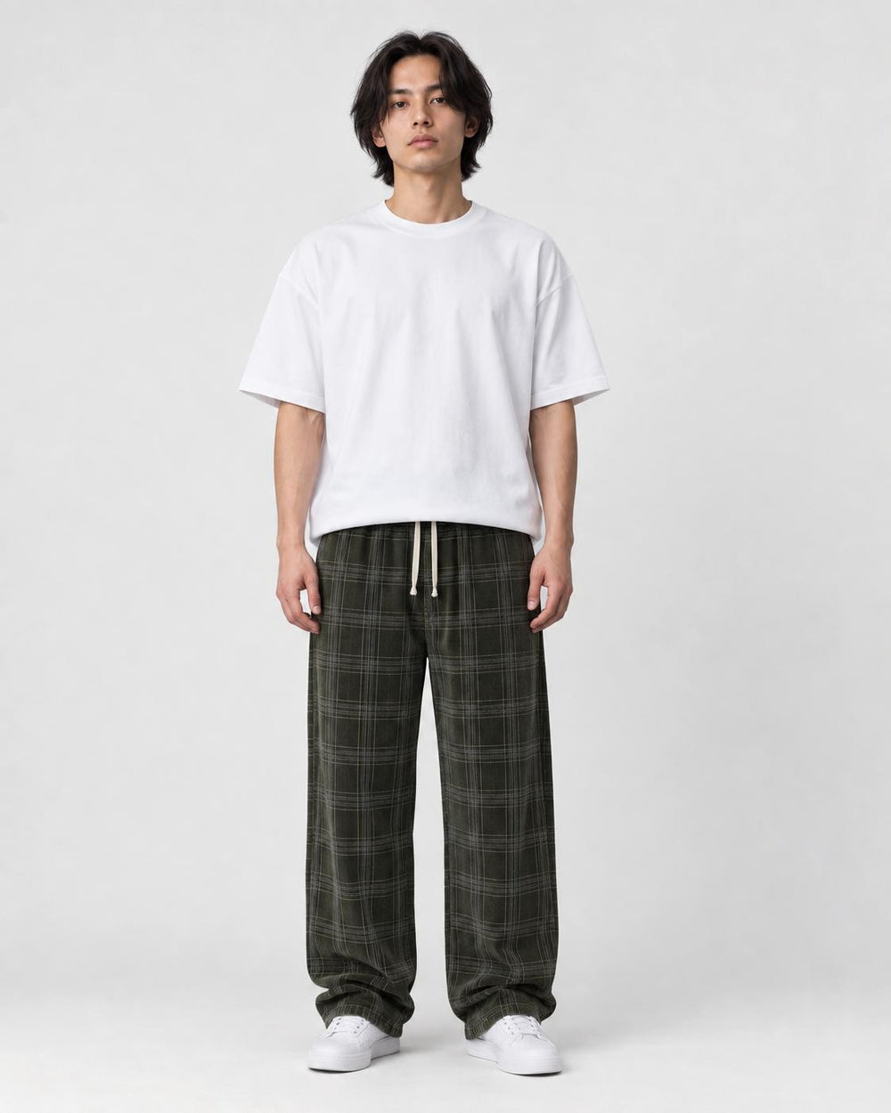 Man in army green plaid wide-leg drawstring pants, white tee and white sneakers, full length