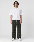 Man in army green plaid wide-leg drawstring pants, white tee and white sneakers, full length