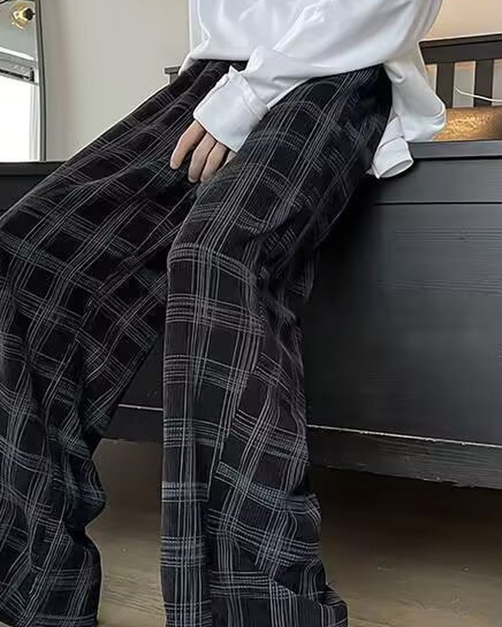 Black plaid wide-leg pants worn seated on a bed, thigh to shin