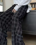 Black plaid wide-leg pants worn seated on a bed, thigh to shin