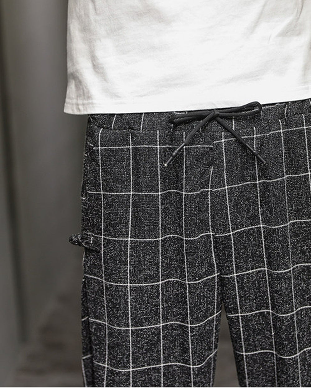 Close-up of the elastic drawcord waist and a frog-button knot on the black plaid harem pants