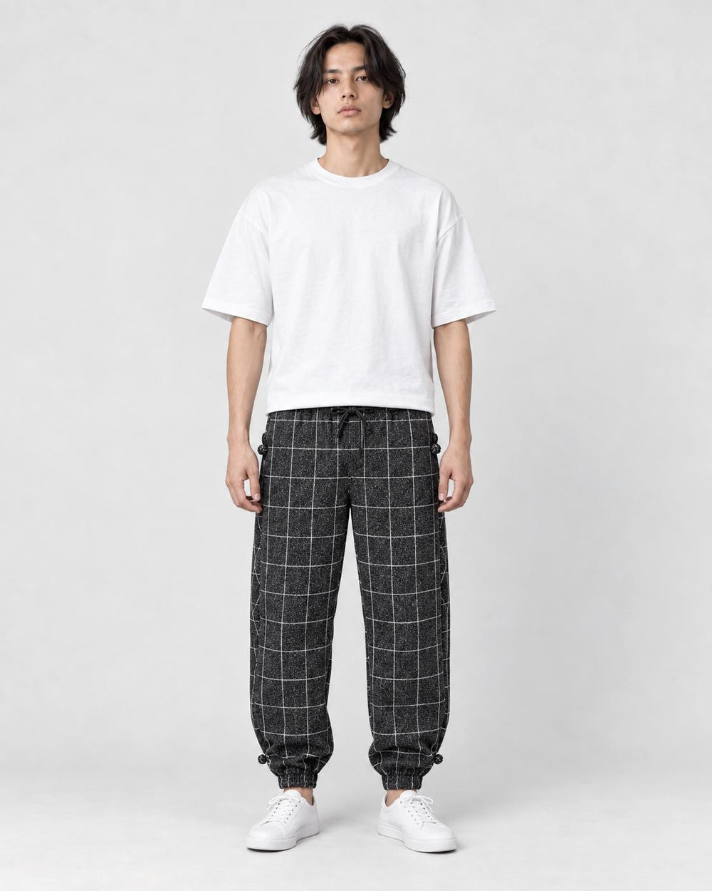 Model wearing the black plaid harem pants with a white tee and white sneakers, front view
