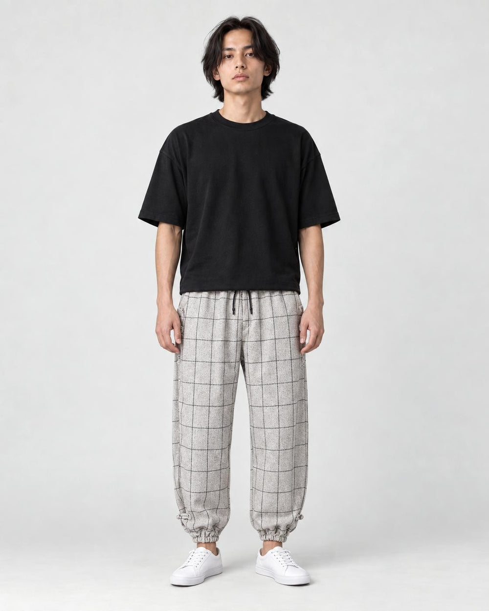 Model wearing the cream plaid harem pants with a black tee and white sneakers, front view