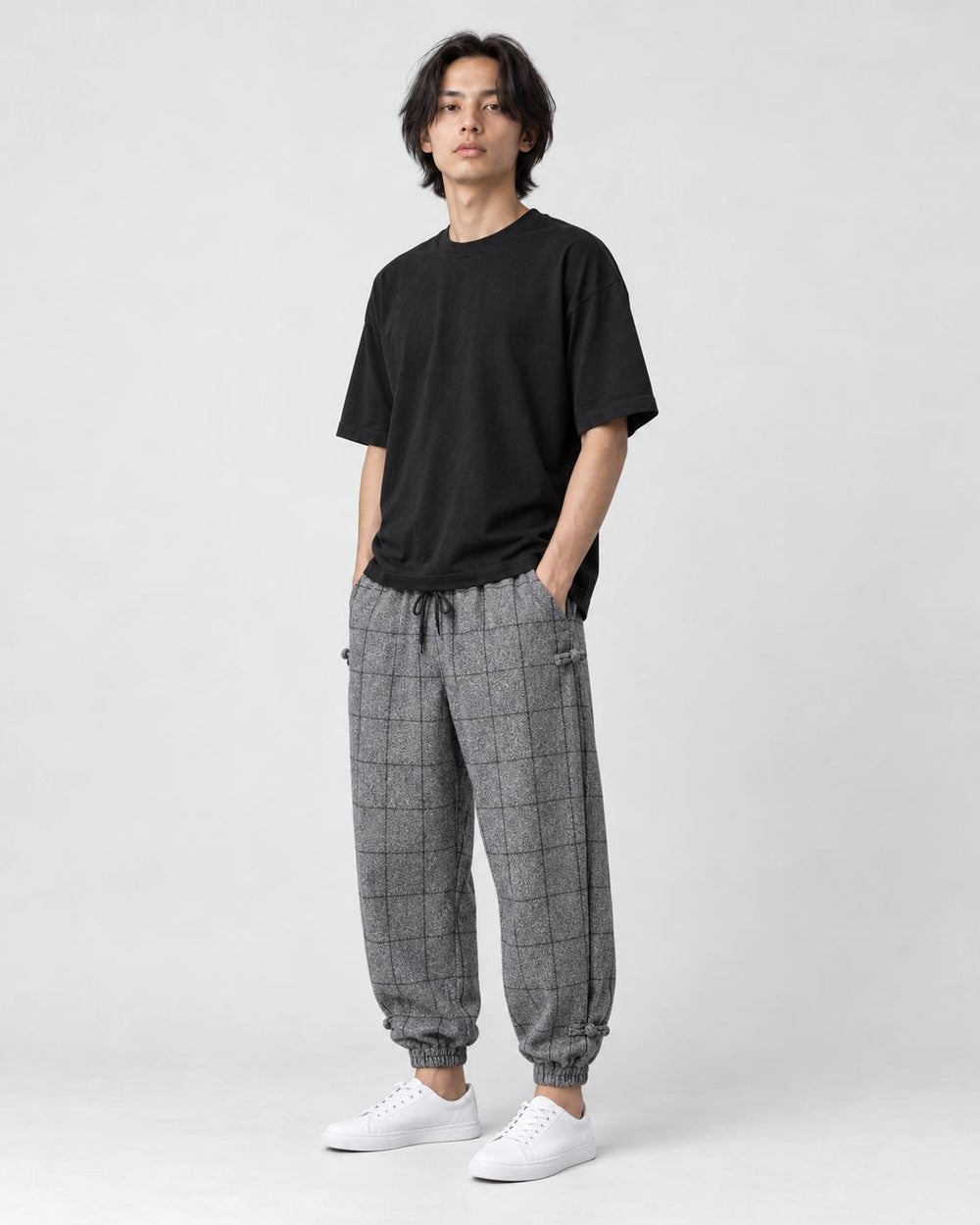 Model wearing the gray plaid harem pants with a black tee and white sneakers, three-quarter view