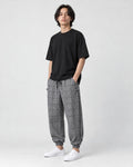 Model wearing the gray plaid harem pants with a black tee and white sneakers, three-quarter view