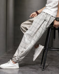 Man seated on a stool in the cream plaid harem pants, showing the frog-button knots at the hip and cuff