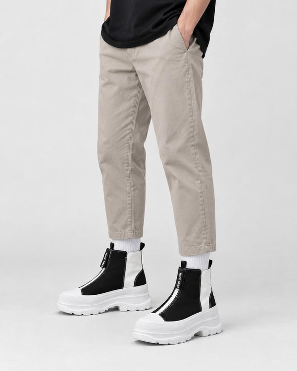Legs of a man in the black and white platform sneaker boots with a front zip, stone trousers and white socks