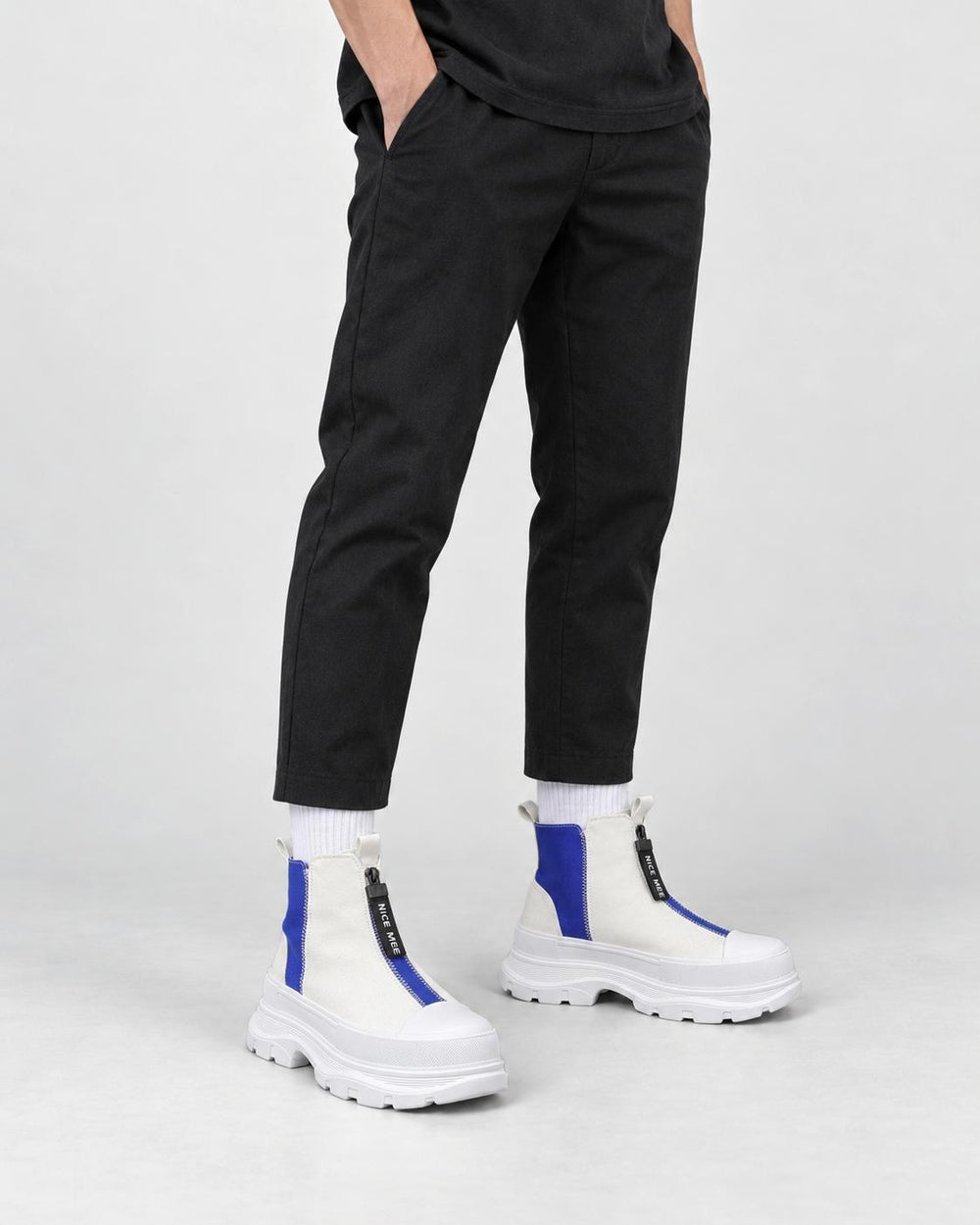 Legs of a man in the blue and white platform sneaker boots with a front zip, black trousers and white socks