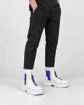 Legs of a man in the blue and white platform sneaker boots with a front zip, black trousers and white socks