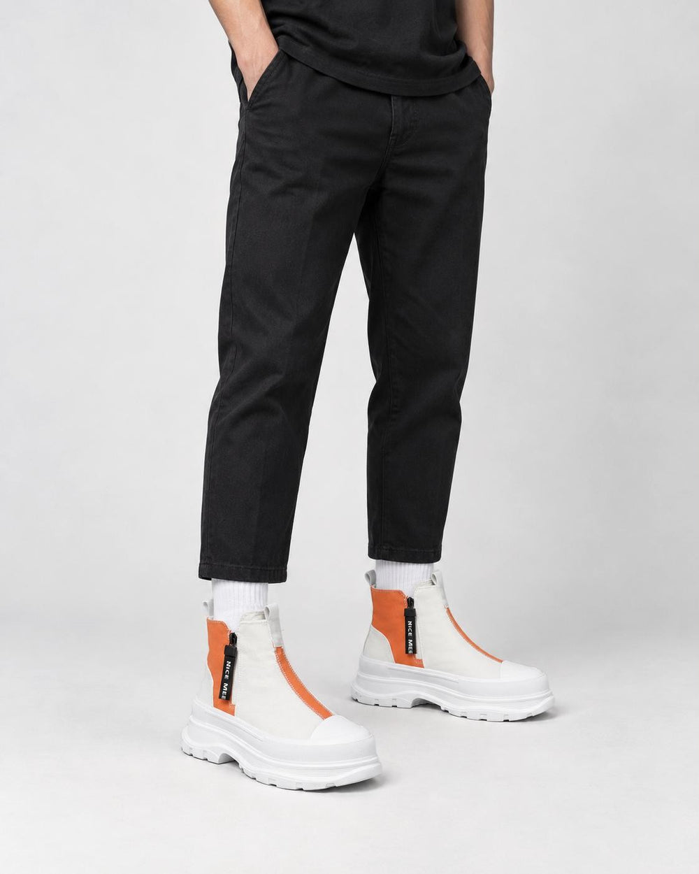 Legs of a man in the orange and white platform sneaker boots with a front zip, black trousers and white socks