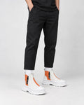 Legs of a man in the orange and white platform sneaker boots with a front zip, black trousers and white socks