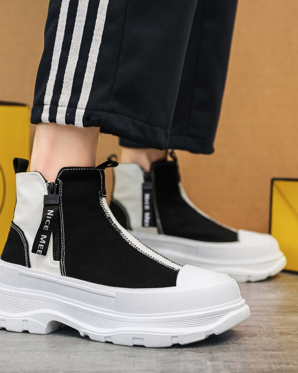 Black and white platform sneaker boots on foot with black striped track pants, three-quarter view