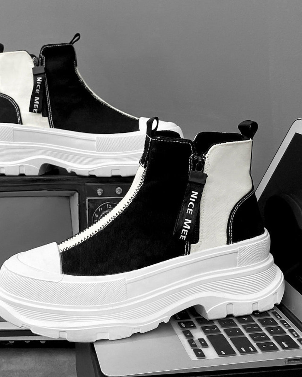 Black and white platform sneaker boots from the side, showing the white zig-zag zip tape and the NICE MEE pull
