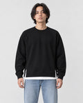 Model wearing the black raglan sweatshirt with a white layered hem and light-wash jeans, front view