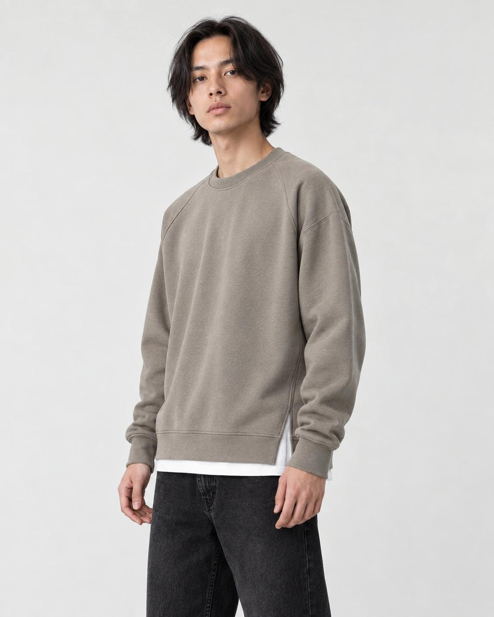 Model wearing the taupe raglan sweatshirt with a white layered hem and black trousers, three-quarter view