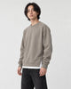 Model wearing the taupe raglan sweatshirt with a white layered hem and black trousers, three-quarter view