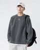 Dark gray raglan sweatshirt worn with a black backpack, showing the side slit and the white layered hem