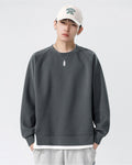 Dark gray raglan sweatshirt with a white layer showing below the hem, worn with a white cap and gray pants