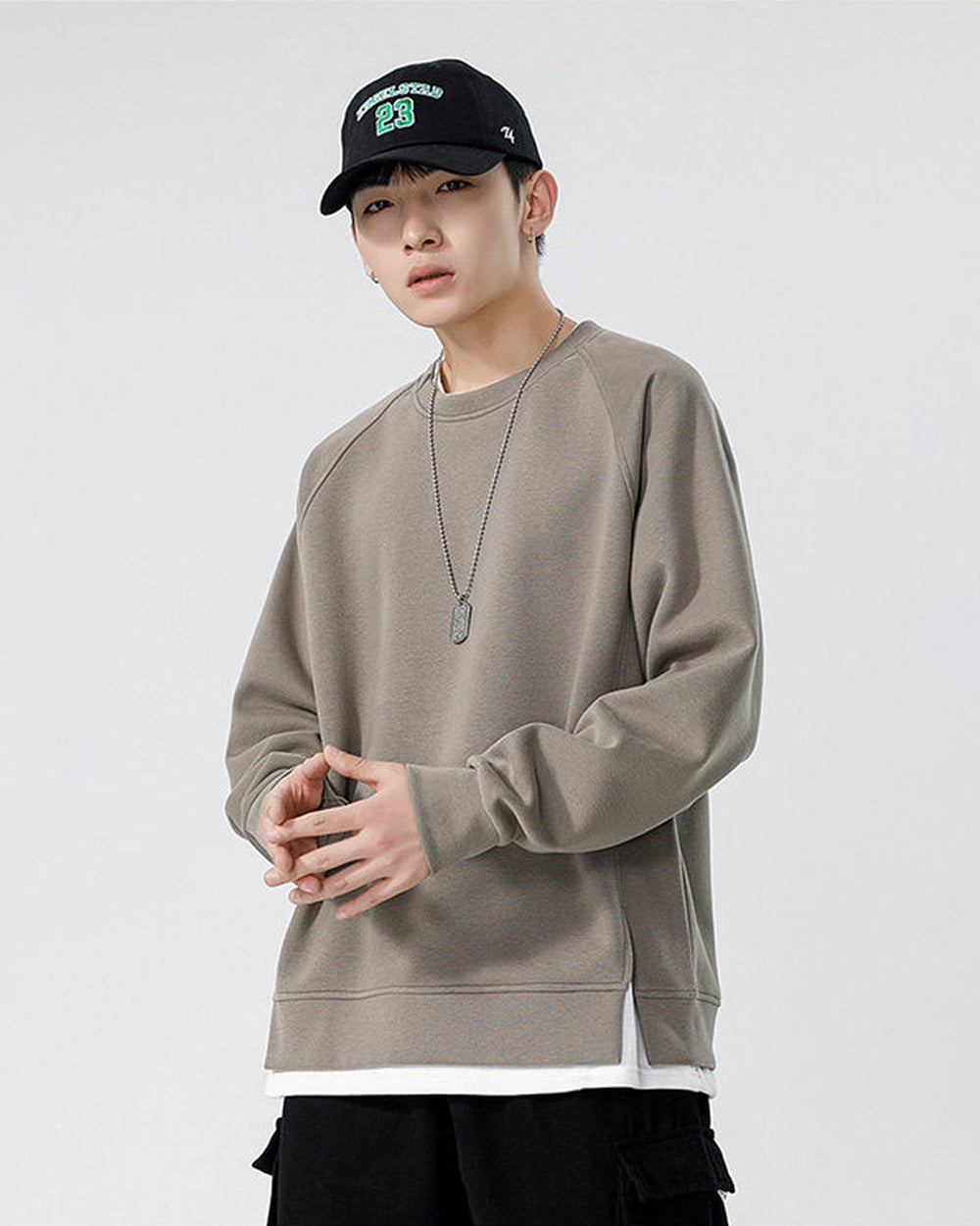 Taupe raglan sweatshirt with a white layer at the hem, worn with a black cap and black cargo pants