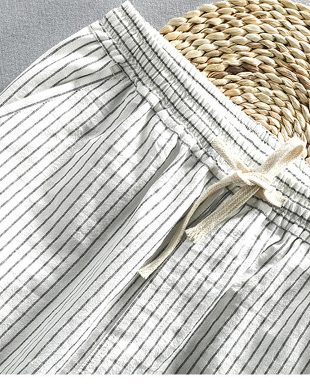 Close-up of the elastic waistband and the cream drawstring tied in a bow on the white striped pants