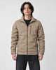Model wearing the khaki windbreaker jacket over a black tee with black jeans and white sneakers, three-quarter crop