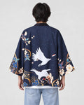 Man seen from behind in the dark navy haori with two white cranes in flight and blue flowers at the hem, over a white tee