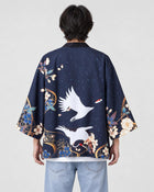 Man seen from behind in the dark navy haori with two white cranes in flight and blue flowers at the hem, over a white tee