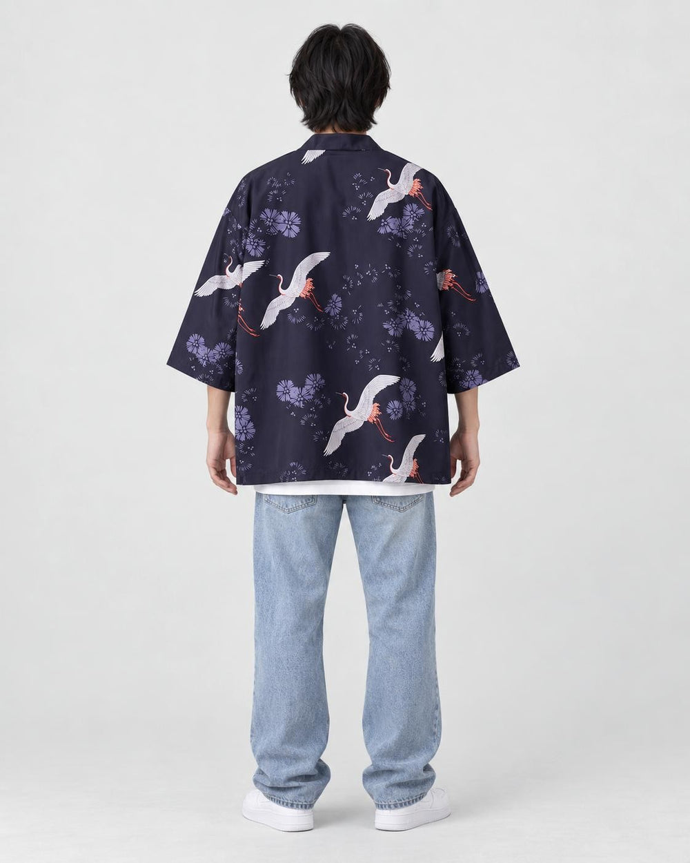 Full-length back view of a man in the dark navy haori with white cranes and lilac flowers, worn with light jeans