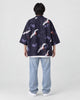 Full-length back view of a man in the dark navy haori with white cranes and lilac flowers, worn with light jeans