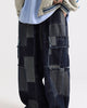 Indigo patchwork cargo pants worn with a cream varsity jacket, three-quarter view showing the flap pockets