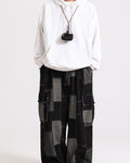 Black patchwork denim cargo pants with gray patches and white stitching, worn with a white hoodie, front view