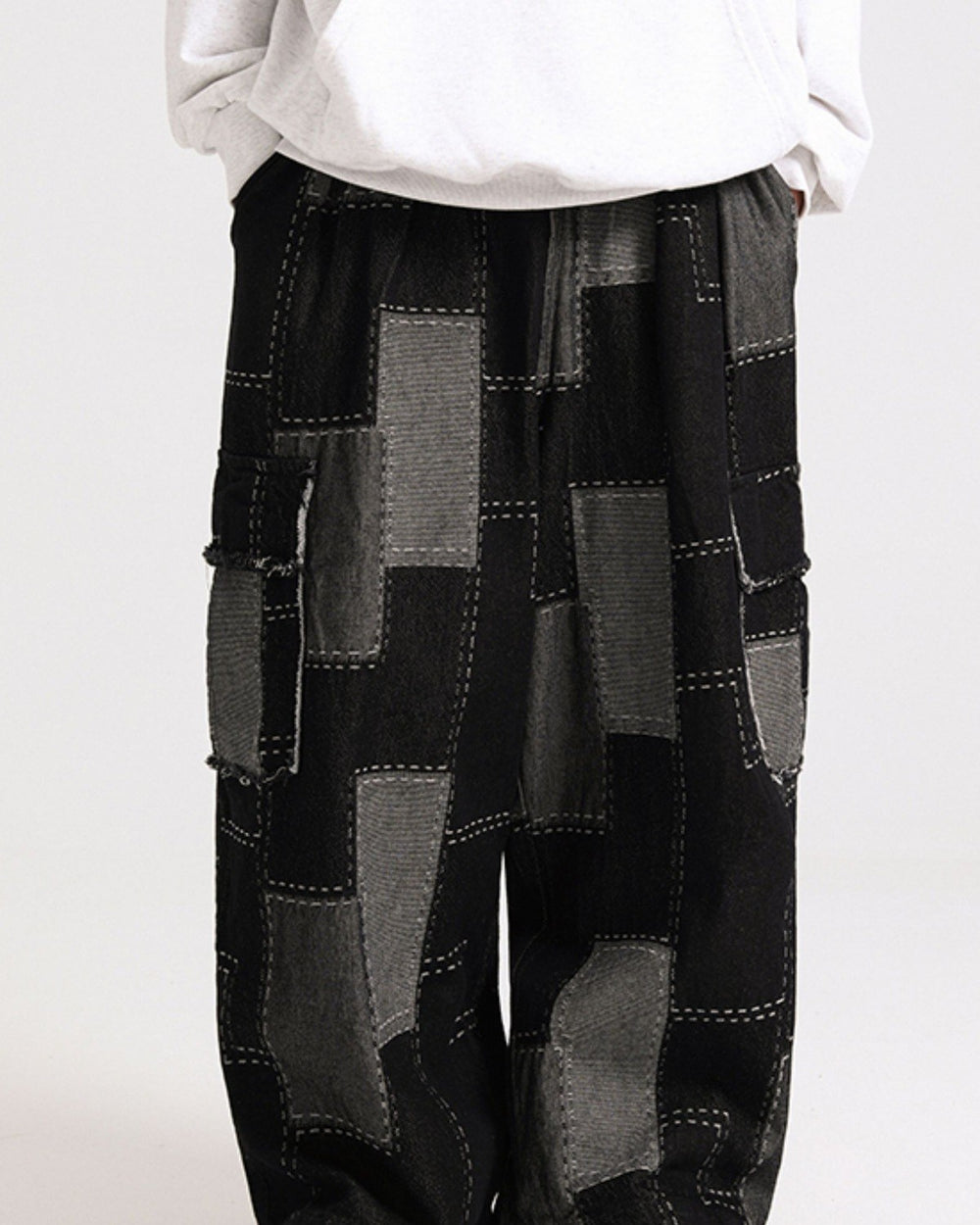 Black patchwork cargo pants seen from the waist down, with gray patches joined by white running stitches
