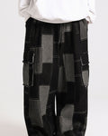Black patchwork cargo pants seen from the waist down, with gray patches joined by white running stitches