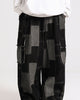 Black patchwork cargo pants seen from the waist down, with gray patches joined by white running stitches