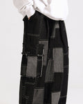Black patchwork cargo pants in three-quarter view, with the large flap pocket on the outer leg